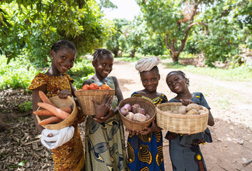 Four smart young African girls with straw baskets full of vegetables, on their way to the local...