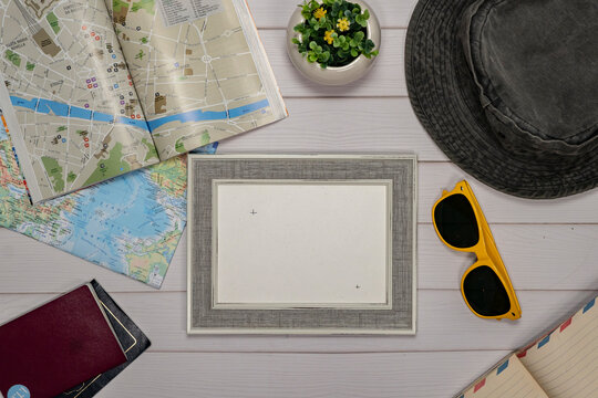 Travel Flat lay of an empty frame, sunglasses, passport, camera and a map over a white wooden table