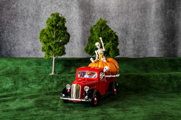 two skeletons in red pickup truck with large pumpkin waving