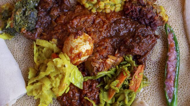 Zoom out of Injera served with chicken, egg, doro wat, berbere, vegetables and lentils. Injera, a traditional staple food of Ethiopia, is a sourdough flatbread made from teff flour.