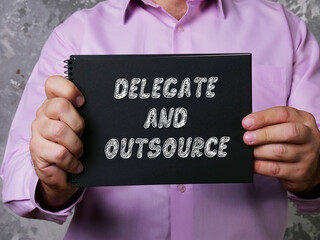 Financial concept meaning DELEGATE AND OUTSOURCE with inscription on the piece of paper.