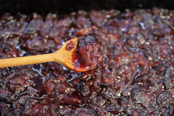 Boiled plums in a wooden spoon at home in the kitchen. The process of making plum jam