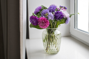 bouquet of colorful asters in vase is on the windowsiil