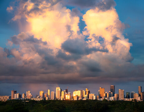 Dramatic panorama view of large rain storm cloud during sunset over Miami skyline with golden hour light reflecting off glass buildings taken from distant vantage near Coral Gables in South Florida