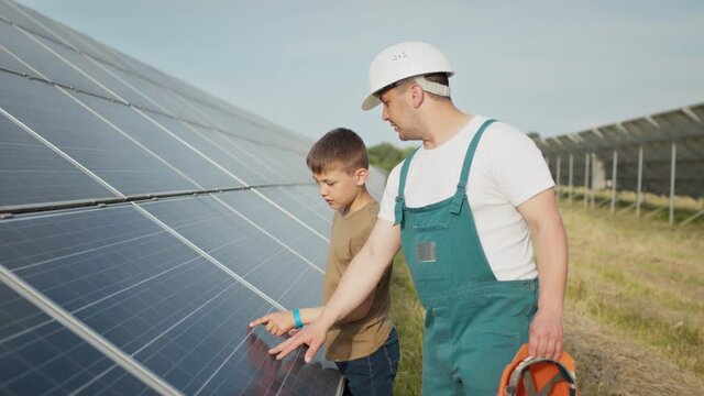 An young engineer father is explaining to his little son an operation and performance of photovoltaic solar panels at sunset. Concept: renewable energy, technology, electricity, green, future, family.