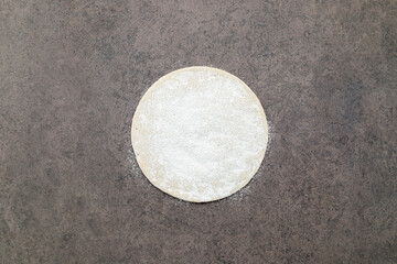 Obraz premium Thin homemade pizza dough with scattered wheat flour on dark concrete background.