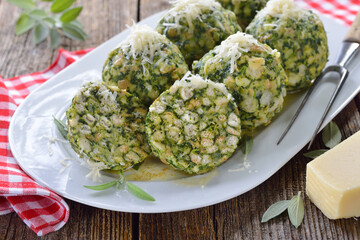 Deftige hausgemachte Südtiroler Spinatknödel mit gebräunter Salbei-Butter und Parmesen auf weißer Platte serviert - South Tyrolean spinach bread dumplings with melted sage butter and parmesan cheese