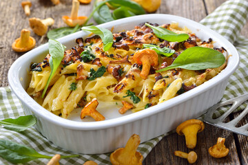 Nudelauflauf mit frischen Pfifferlingen und Blattspinat heiß aus dem Backofen serviert – Chanterelle pasta casserole with spinach leaves and cheese served hot from the oven