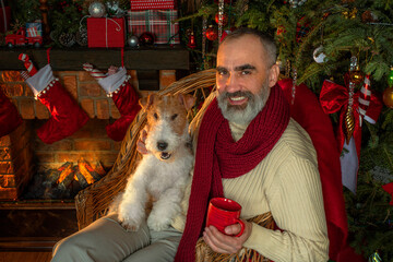 Santa Claus with dog near fireplace and Christmas tree. Festive interior inside wooden house, New...