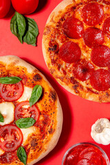 Homemade margherita and pepperoni pizza with fresh basil and garlic on a bright red background