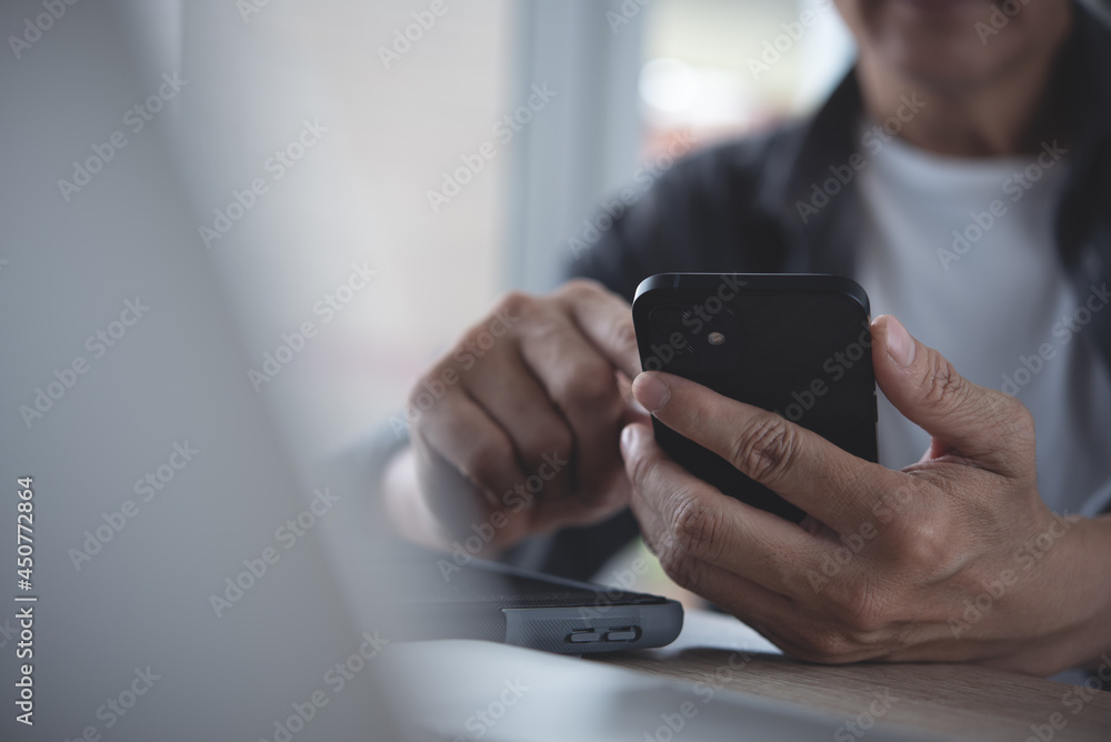 Poster asian man using mobile smart phone during online working on laptop computer on table in modern home 