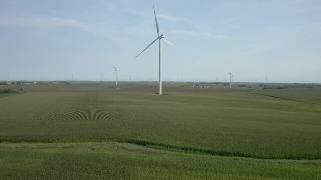 Aerial 4k video of a farm of wind turbines producing green energy on a sunny summer day in Iowa.