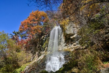 Fototapeta na wymiar 青空バックに見上げるちょうど見頃の紅葉に囲まれた乙女の滝の情景＠蓼科、長野