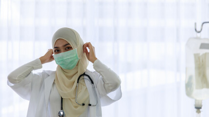 Portrait of young female muslim doctor put on face mask for protection of infective disease in hospital. Covid-19 pandemic concept