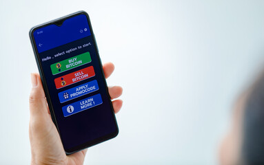 Hand holding and showing smartphone screen with buy and sell and promotion code buttons in cryptocurrency trading application with copy space