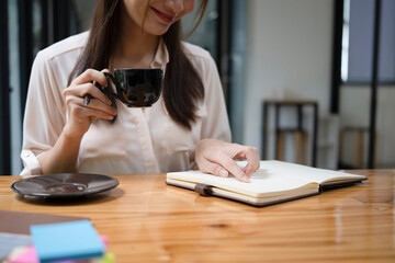 Smiling young woman drinking hot coffee and reading book at home.