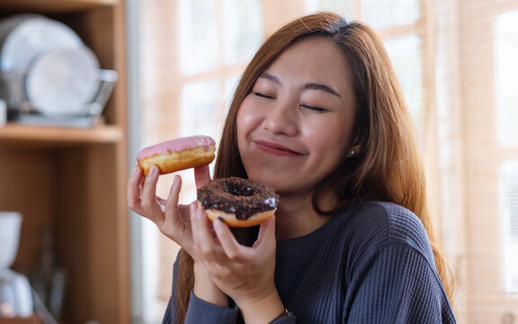 Portrait image of a beautiful young asian woman holding and enjoyed eating donuts at home