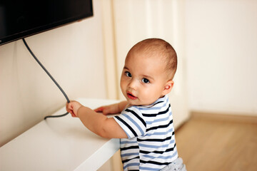 Sweet naughty baby boy pulls the electric cord from the TV