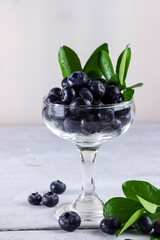 Freshly picked blueberries in a bowl. Juicy and fresh blueberries with green leaves on rustic table. Concept for healthy eating and nutrition