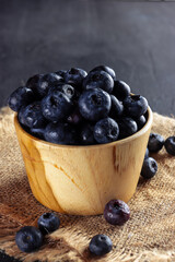 Freshly picked blueberries in a bowl. Juicy and fresh blueberries with green leaves on rustic table. Concept for healthy eating and nutrition