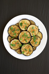 Homemade Organic Roasted Eggplant on a white plate on a black surface, top view. Flat lay, overhead, from above.