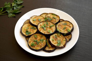 Homemade Organic Roasted Eggplant on a white plate on a black background, side view.