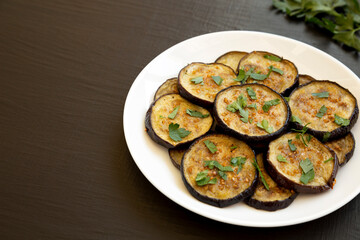 Homemade Organic Roasted Eggplant on a white plate on a black surface, side view. Copy space.