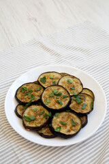 Homemade Organic Roasted Eggplant on a white plate on a white wooden background, side view. Copy space.