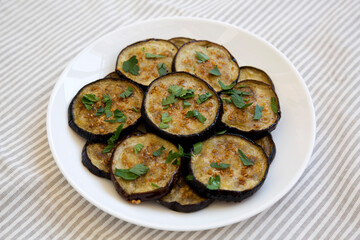 Homemade Organic Roasted Eggplant on a white plate on a white wooden background, side view.