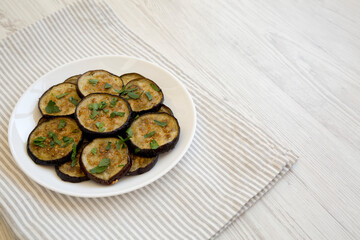 Homemade Organic Roasted Eggplant on a white plate on a white wooden background, side view. Copy space.