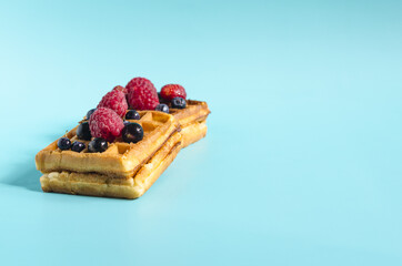Fresh waffles with different berries of black and red color on a blue background hard light. Homemade cakes crispy waffles on a colored background copy space