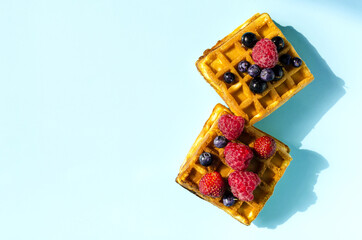 Fresh waffles with different berries of black and red color on a blue background hard light. Homemade cakes crispy waffles on a colored background copy space