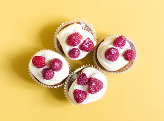 Cupcakes with white cream and raspberries on a yellow background. Sweet homemade cakes close-up on a colored background.