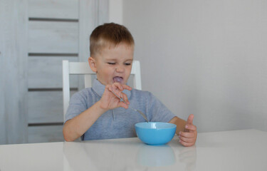 Child does not want to eat and pushes plate away, a little boy is in kitchen. A sad child does not want to eat porridge. A little boy eats without appetite. TConcept of healthy breakfast for children