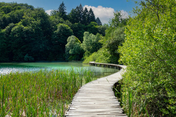 Fototapeta na wymiar Wooden walkway is crossing a gorgeous lake in a tourist attraction in Croatia.