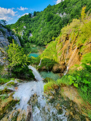 Fototapeta na wymiar VERTICAL: Shot from the top of a waterfall overlooking emerald ponds of Plitvice