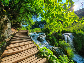 LENS FLARE: Wooden steps lead up to the top of a sunlit waterfall in Plitvice.