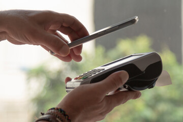 Contactless payment from a smartphone to a TPV terminal . Detail of hands and electronic devices