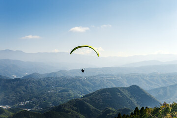 A yellow paraglider is flying over the mountain