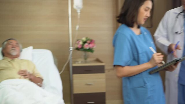 asian young doctor man talking with  nurse woman using digital tablet Analysis of senior patient symptoms sleeping on bed  in hospital.