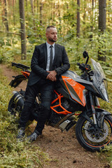 Fototapeta na wymiar Handsome man in costume with dark motorcycle in woods