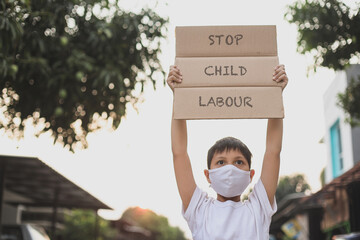 Asian boy in medical mask raising letter board says Stop Child Labour  campaign