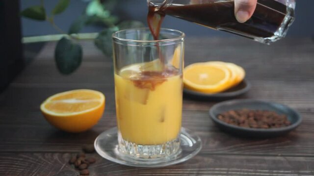 Woman hand preparing bumble coffee cocktail with espresso and fresh orange juice.
