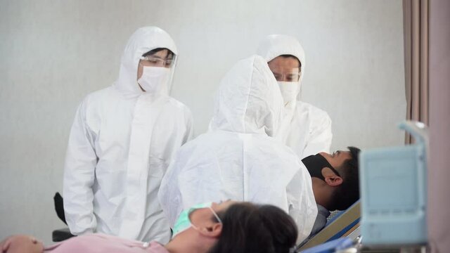 group of asian doctor wearing  ppe suit is currently examining the infection and treating patients coughing  from coronavirus or covid 19 on bed in quarantine room at hospital . flu outbreak