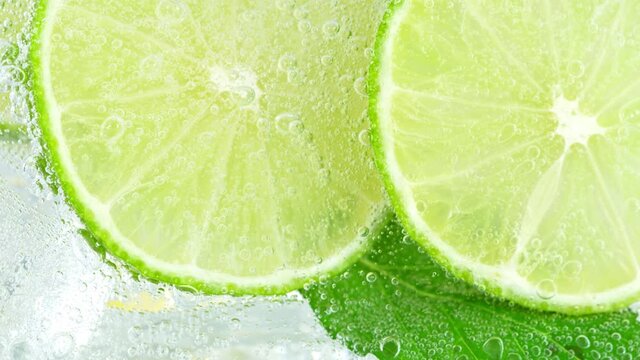 Super Slow Motion Shot of Pouring Water on Lime Slices and Ice Cubes in Glass at 1000 fps.