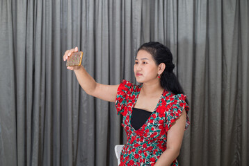 A young beautiful woman in her 20s, dressed well and taking selfie indoor at home. Social influencer smiles at her smartphone as she takes selfie of herself. 