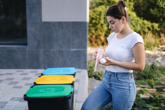 Woman throwing out in recycling bin washed and empty shampoo and deodorant bottles. Female looks at the packages to find out in wich recycling bin throw the garbage