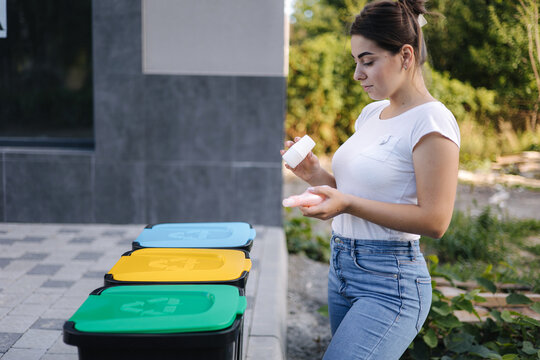 Woman throwing out in recycling bin washed and empty shampoo and deodorant bottles. Female looks at the packages to find out in wich recycling bin throw the garbage