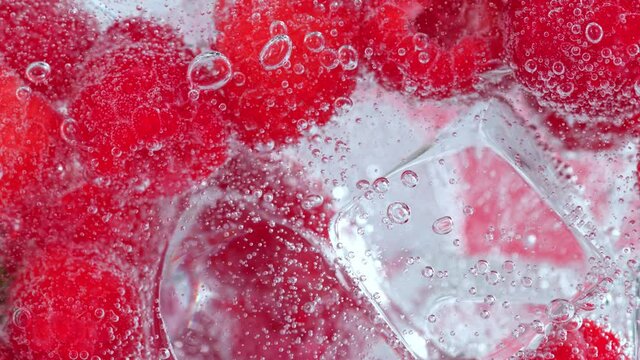 Super Slow Motion Shot of Fizzing Water with Raspberries and Ice Cubes in Glass at 1000 fps.