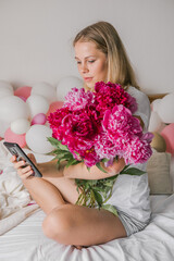Image of a happy positive pretty young woman indoors at home  in bedroom in bed holding flowers take a selfie by mobile phone.
